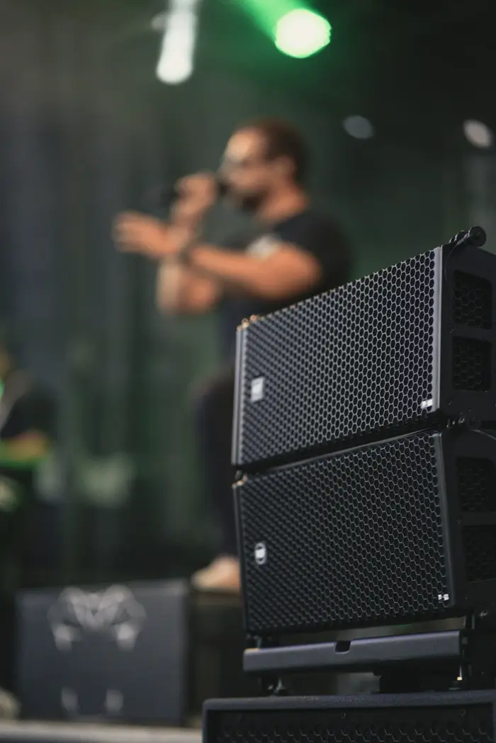 A stack of line array loudspeakers beside a performer on stage.
