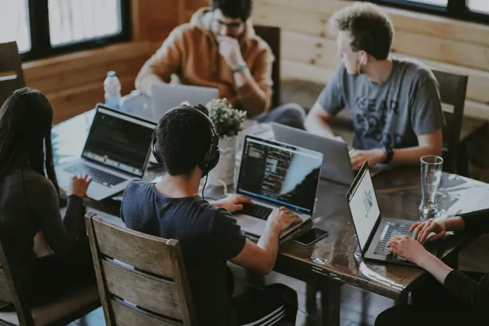 Colleagues working together around a table with laptops open.