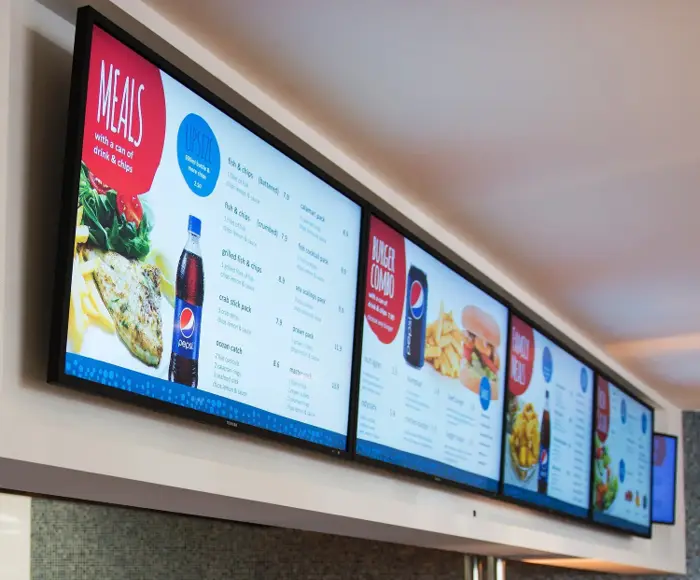 A row of wall-mounted digital menu screens in a cafe.